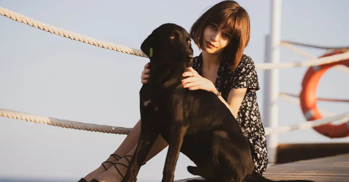 Woman sitting outdoors with black dog wearing a smart QR pet ID tag by the sea