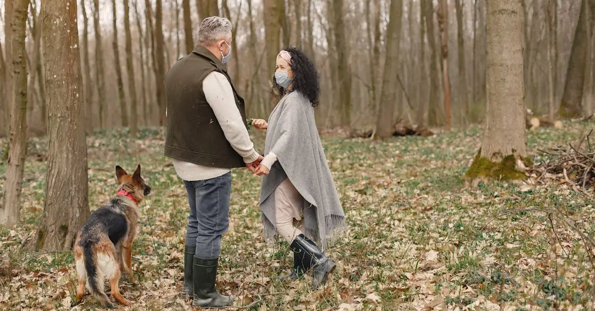 Couple wearing masks walking dog in a UK forest, holding hands, pet safety concept
